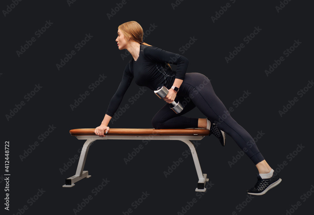 Obraz premium Beautiful young woman trains deltoid on bench in gym isolated on black