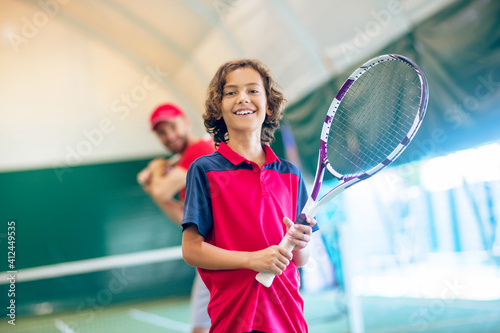 Cute dark-haired boy standing with a tennis racket and smiling