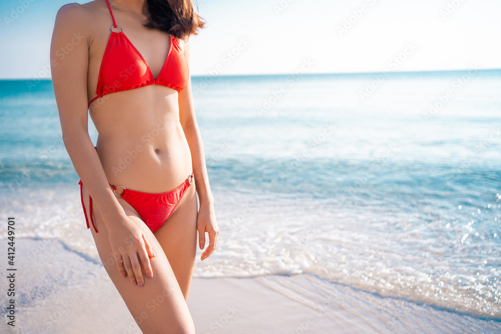 Woman with perfect body in red bikini on sea background. She is taking a walk by the sea.