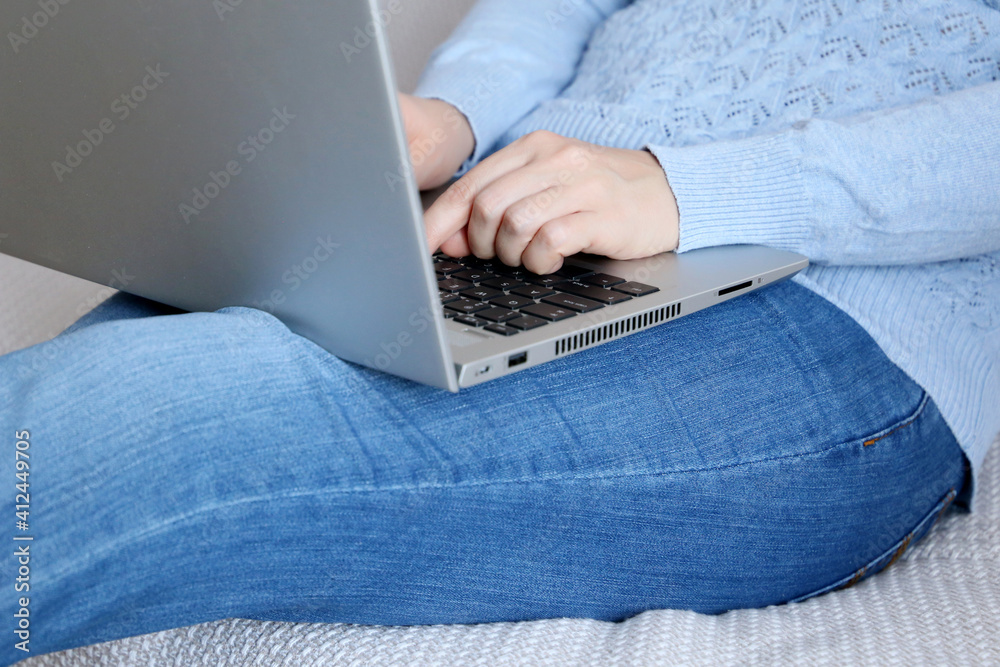Fototapeta premium Woman in jeans sitting with laptop on a sofa, remote work at home. Concept of working on a computer at cozy atmosphere