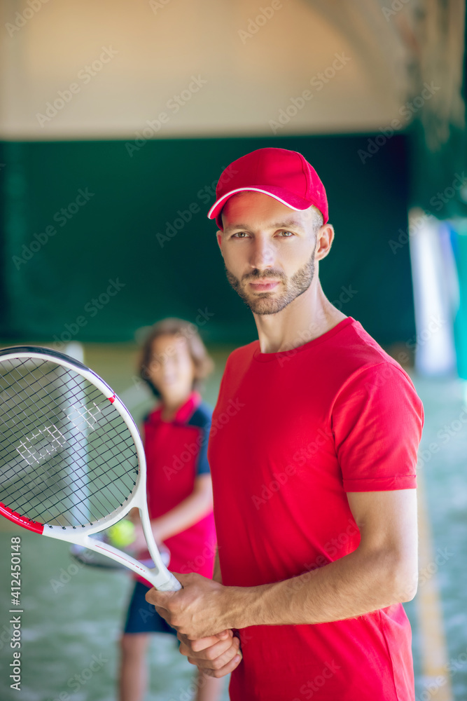 Young bearded man in a red cap standing with a tennis racket
