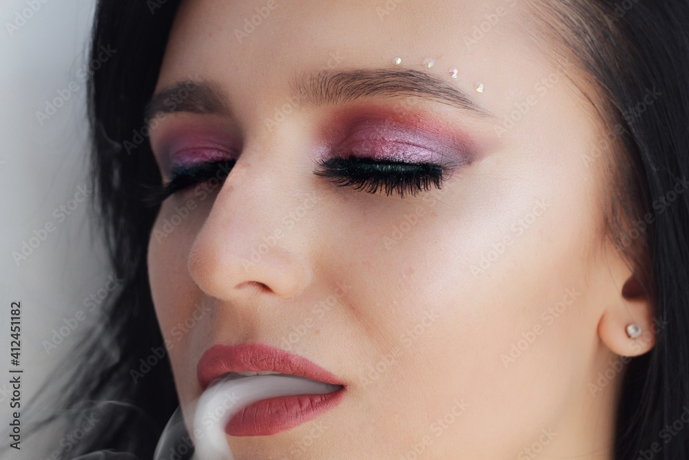 Beautiful young brunette model with bright make-up and long hair. Close up smoke