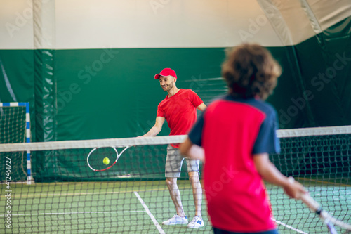 Coach in red clothes and cap playing tennis with a boy © zinkevych