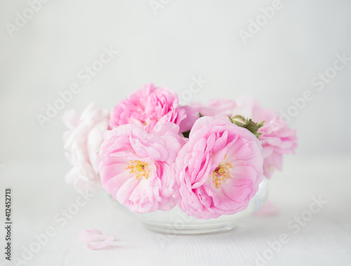 Bouquet of small light pink Roses in a glass vase against of pale grey wooden background. Selective focus. Shallow depth of field.