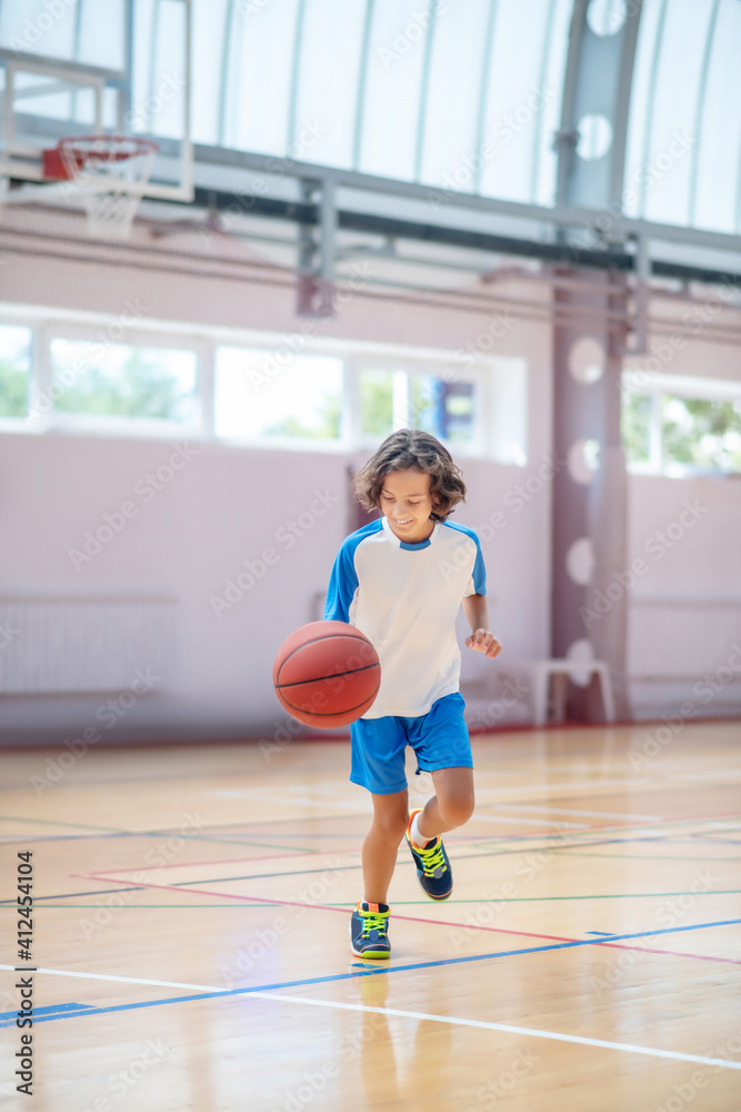 Boy in sportswear running after the ball in a gym