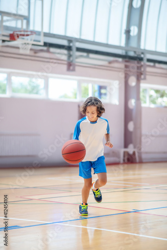 Boy in sportswear running after the ball in a gym