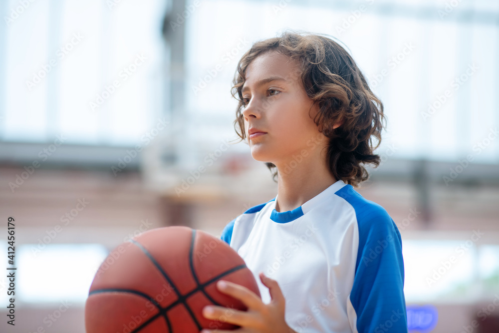 Dark-haired boy in sportswear holding a ball and looking serious Dark-haired boy in sportswear holding a ball and looking serious