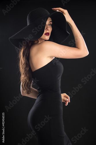fashion portrait of a young and very beautiful girl in a black hat on a black background