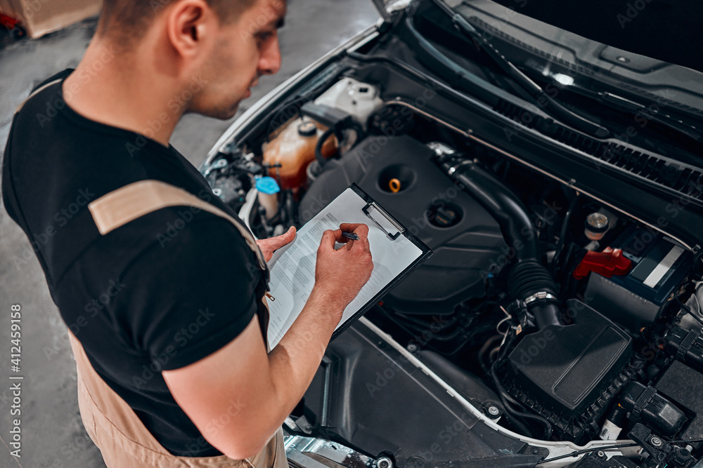 Man in technician uniform going to repair for car maintenance and make notes.