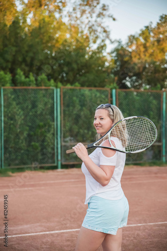 gorgeous blonde in blue shorts standing with a tennis racket on a Sportsground