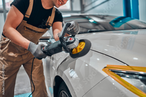Photography Professional auto detailer hand holding rotary polisher while polishing paint surface of shiny white car