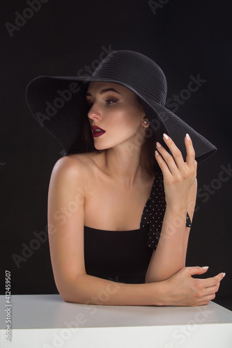 fashion portrait of a young and very beautiful girl in a black hat on a black background
