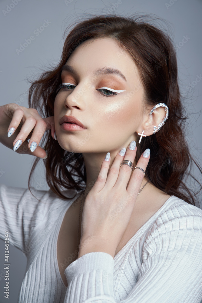 Beauty portrait of a woman with natural makeup and painted polished nails on her hand. Rings on the fingers of the hand Beauty portrait of a woman with natural makeup and painted polished nails on her hand. Rings on the fingers of the hand