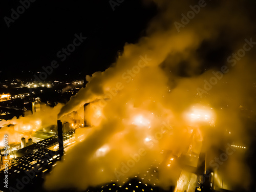Large factory with thick white smoke coming from the chimneys and bright lights from the factory grounds. Blurred image. . High quality photo