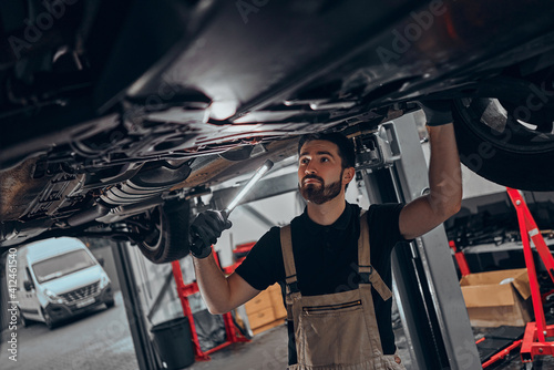 Mechanic shining torch under car at garage. photo