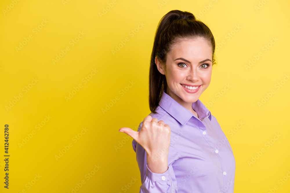 Photo portrait of girl pointing thumb at blank space behind shoulder isolated on bright yellow colored background Photo portrait of girl pointing thumb at blank space behind shoulder isolated on bright yellow colored background