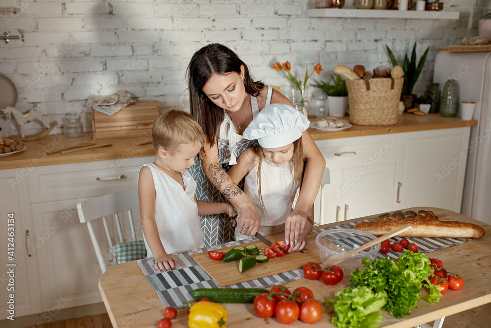 Children learn how to prepare a salad in the kitchen. Family day off, lunch with your own hands. Mom and young cooks