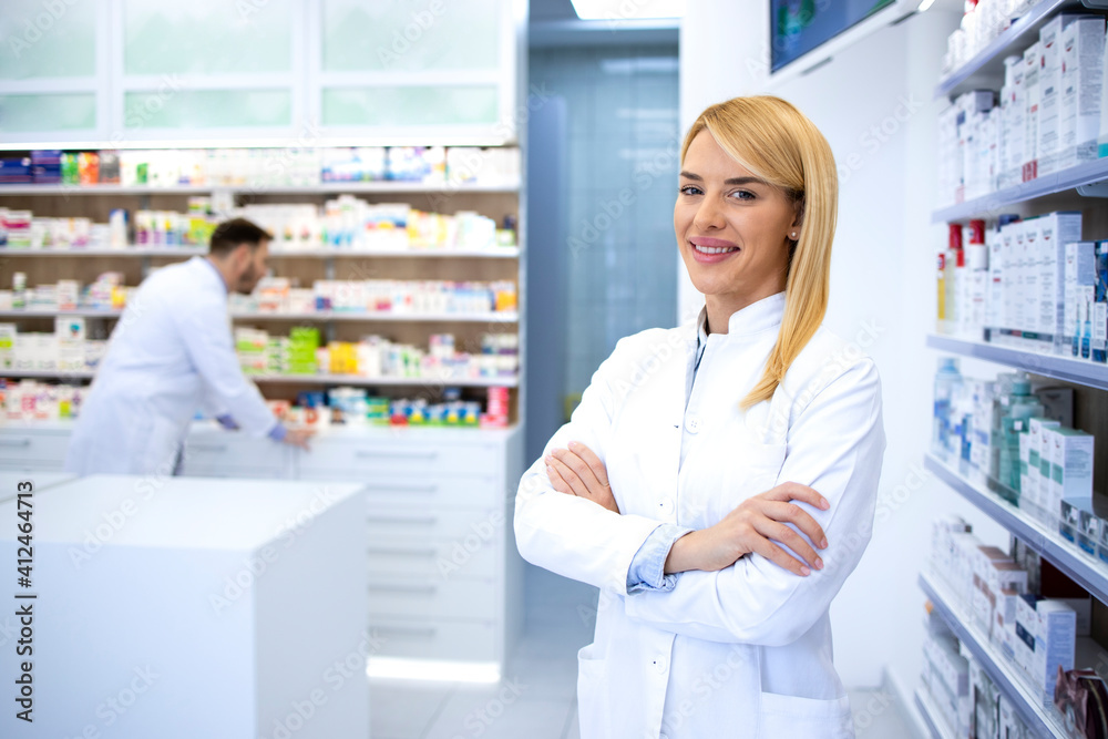 Portrait of professional woman pharmacist proudly standing in pharmacy shop or drugstore. In background shelves with medicines. Healthcare and medicine.