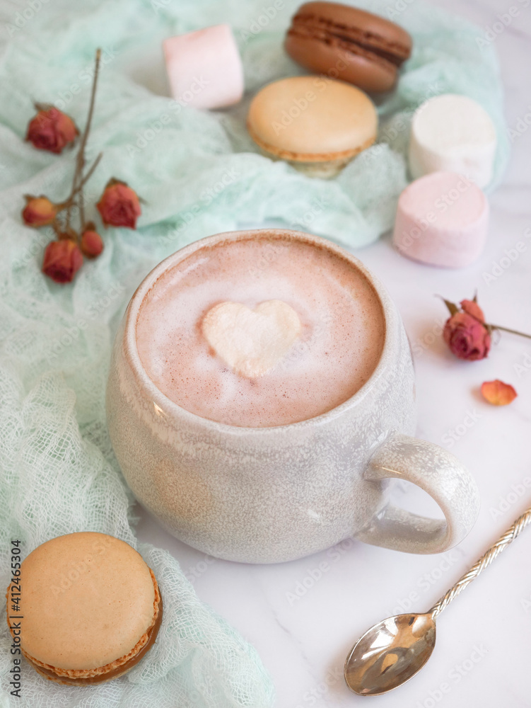 cup of hot chocolate with heart shape marshmallow and pieces of varieties French macarons with dried roses in background. Warming valentine's drink 