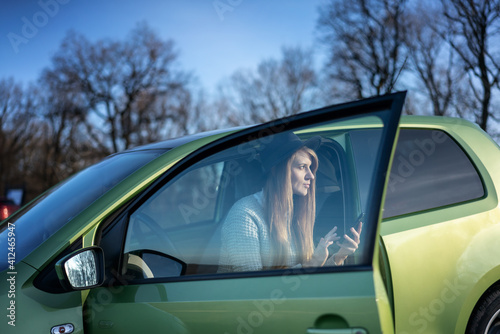 Beautiful young woman wearing hat traveling by car in the countryside while sitting with a smartphone in hands, local travel and adventure concept