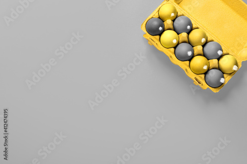 A package of chicken eggs with fluffy white tails like Easter bunnies painted in gray and yellow on a solid grey background with copy space, empty text place. Banner for the religion holiday. Mockup photo