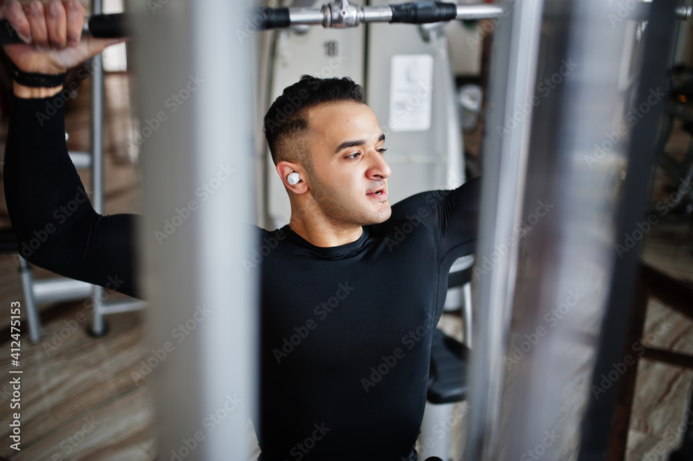 Muscular arab man training and doing workout on fitness machine in modern gym. Muscular arab man training and doing workout on fitness machine in modern gym.