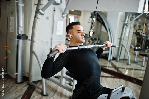 Muscular arab man training and doing workout on fitness machine in modern gym.