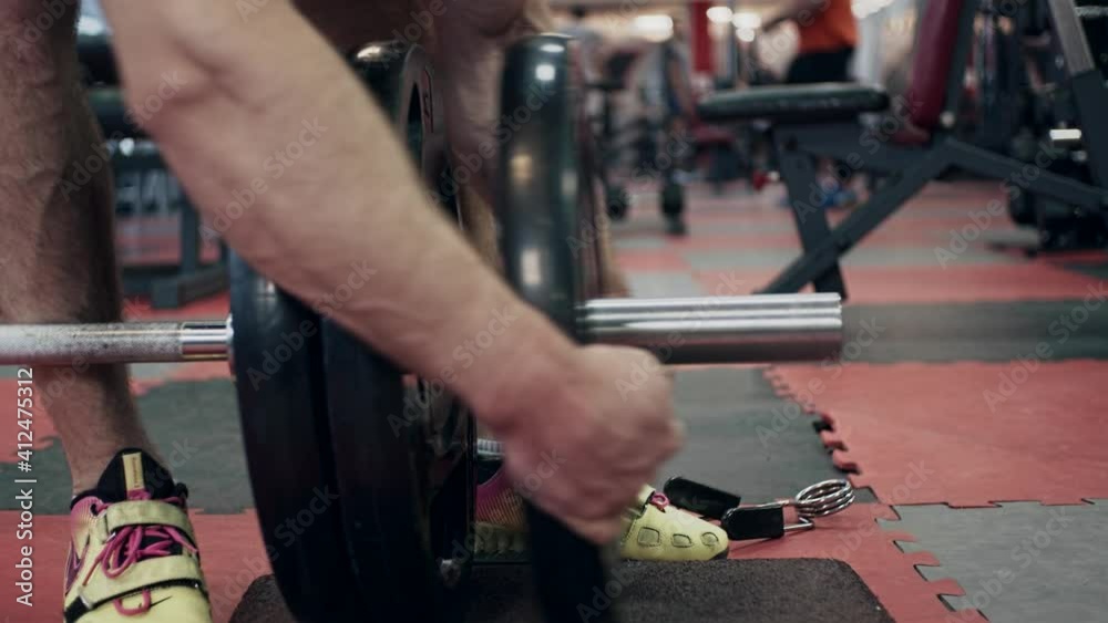 Young powerlifter in gym, adding weight on barbell, slow motion Young powerlifter in gym, adding weight on barbell, slow motion