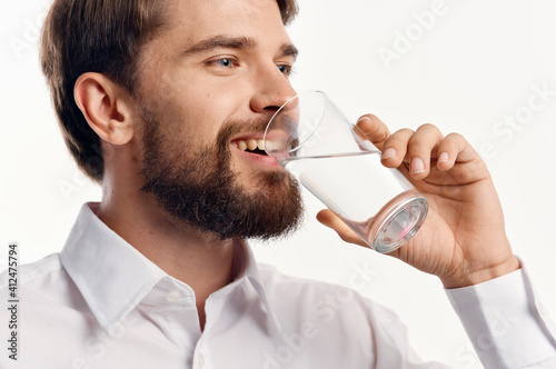 happy man drinks water from a glass on a light background white shirt portrait model