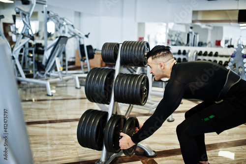Muscular arab man training with dumbbells in modern gym.