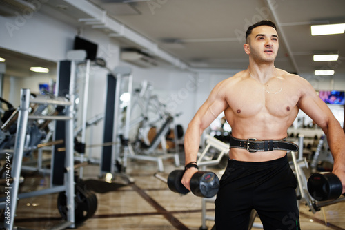 Muscular arab man training in with dumbbells modern gym. Fitness arabian men with naked torso doing workout .