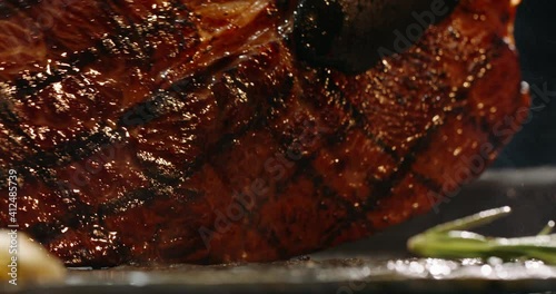 Close up shot of a juicy grilled steak on chef's preparation table. Smoke rising from big piece of tasty meat.