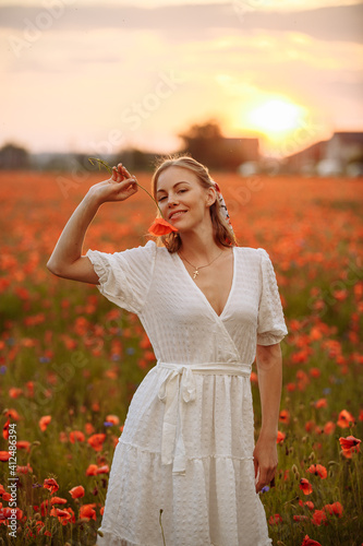 girl in a white dress in a field of poppies on a sunset background