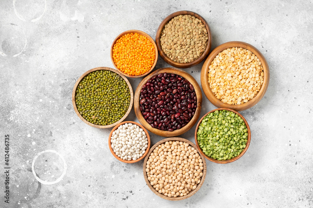 Different legumes. Mung beans, red and white beans, lentils, peas and chickpeas in wooden bowls on the light grey kitchen table. Top view Different legumes. Mung beans, red and white beans, lentils, peas and chickpeas in wooden bowls on the light grey kitchen table. Top view