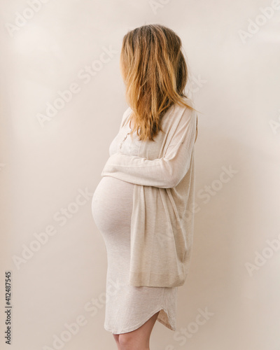 A European caucasian dark blonde pregnant woman in beige neutral outfit holding her belly. photo