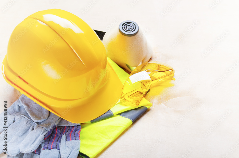 Yellow plastic hard hat, glasses, respirator, reflective vest and protective gloves laying on plywood. Safe labor concept Yellow plastic hard hat, glasses, respirator, reflective vest and protective gloves laying on plywood. Safe labor concept