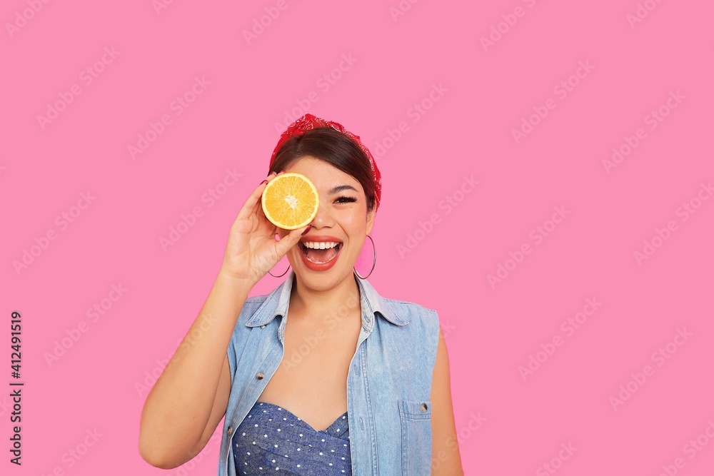 Beautiful smiling young woman in bikini holding fresh orange slice standing over pink background with copy space. Beautiful smiling young woman in bikini holding fresh orange slice standing over pink background with copy space.