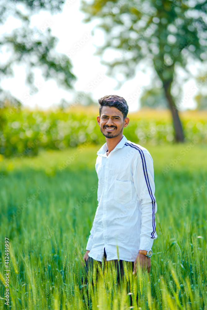 Young indian man standing at green wheat field
