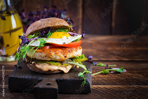Hamburger. Sandwich with chicken burger, tomatoes,  pickled cucumber and fried egg. Fresh tasty chicken burger on wooden table.