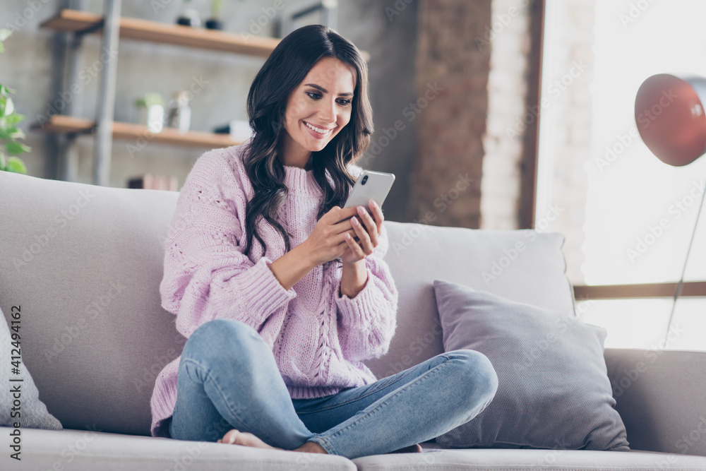 Full body photo of cheerful happy beautiful woman hold phone read message sit couch home inside house Full body photo of cheerful happy beautiful woman hold phone read message sit couch home inside house