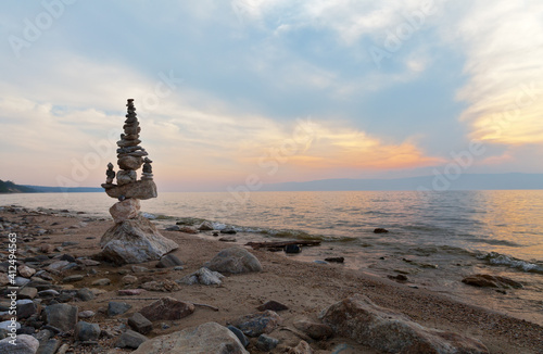 Baikal Lake on a summer evening. Big stone pyramid of tourists on the beach of Olkhon Island against the backdrop of the sunset sky. Summer travel. Beautiful seascape. Calm and harmony concept