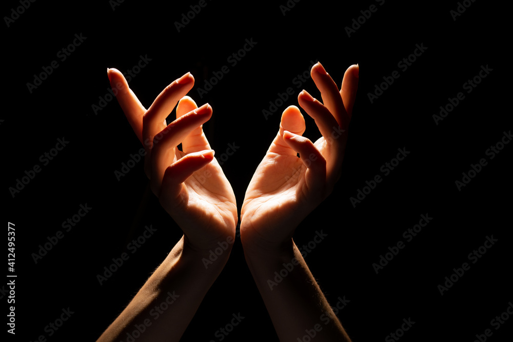 Fototapeta premium Beautiful folded hands with light on top, black background. Prayer or creating a miracle. Hand gestures