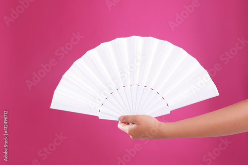 Woman holding white hand fan on pink background, closeup photo