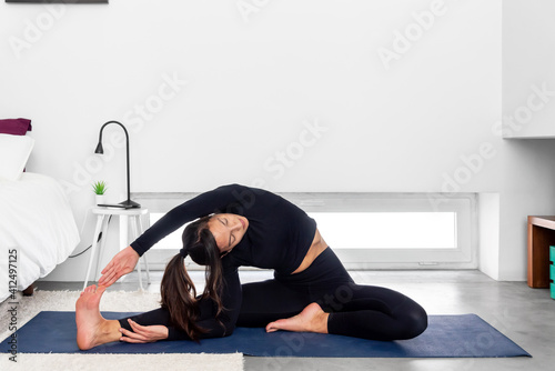 Young slim Woman practicing yoga in modern minimalistic bedroom at home