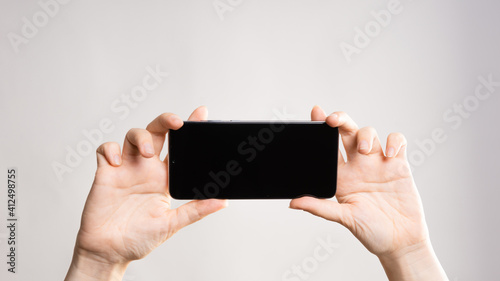 Use your smartphone horizontally, take panoramic photos, or watch videos. Phone in women's hands. Layout for design, mockup. light grey background