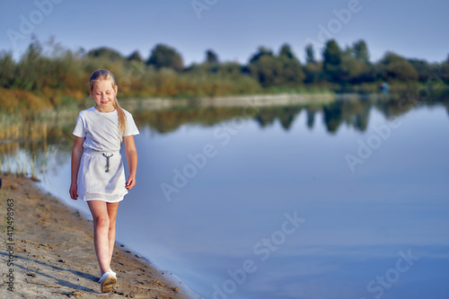 A teenage girl on nature walks along the river bank on a sunny day. © Aleksandr