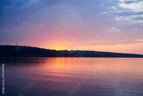 Amazing lake landscape in the evening. Purple orange blue red cloudy sky and setting sun with reflection in water at sunset.Nature protection concept.Rural scene in countryside.Eco tourism development