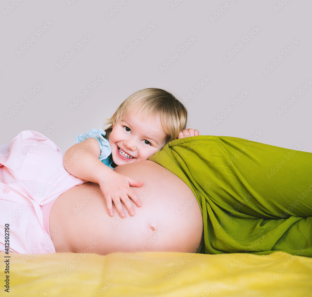 Pregnant mother and daughter together at home. Woman with her first child during second pregnancy. Motherhood and parenting concept. Toddler smiling girl and mom. Happy family expecting for new baby. Pregnant mother and daughter together at home. Woman with her first child during second pregnancy. Motherhood and parenting concept. Toddler smiling girl and mom. Happy family expecting for new baby.