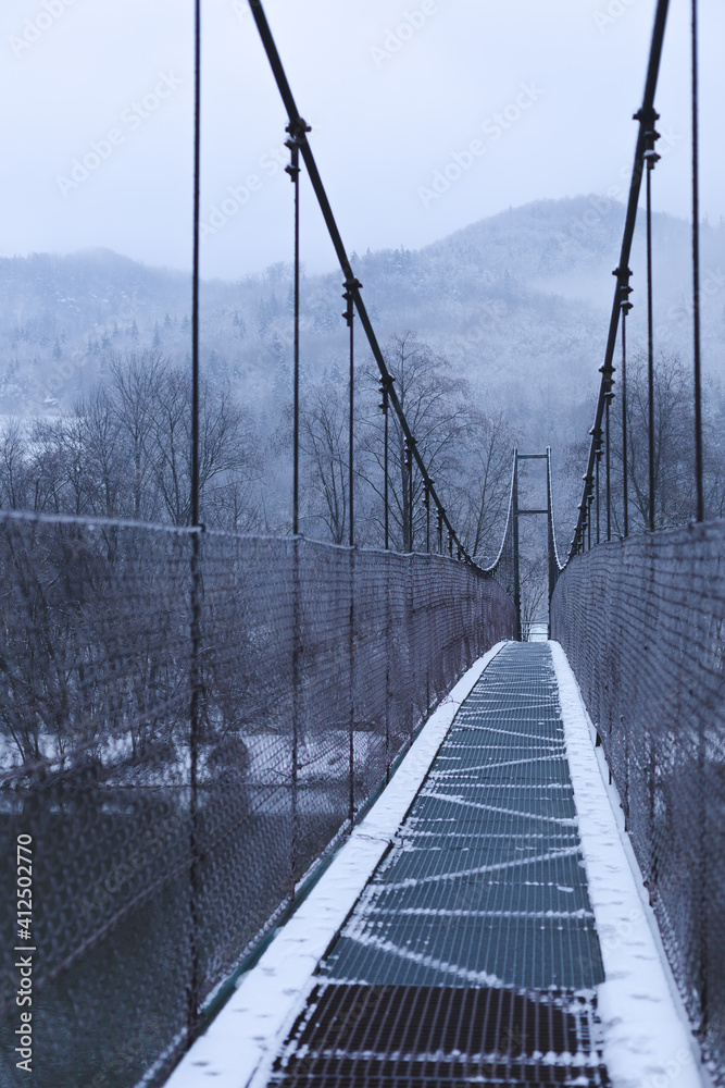 Fototapeta premium Hanging bridge over the river.Mountains in background.Winter image.