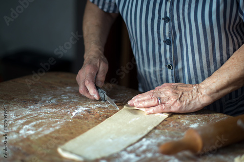 Typical asturian Christmas dessert. Aged woman's hands making casadielles at home. Homemade dough, wooden roller pin and a knife. Gastronomy